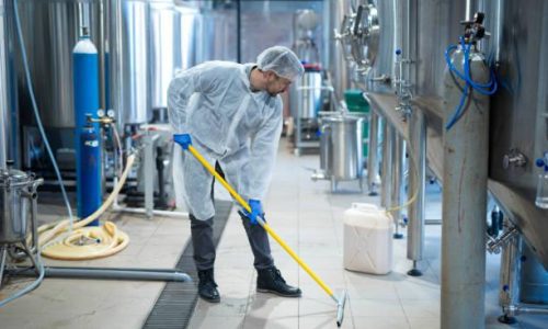 Professional industrial cleaner in protective uniform cleaning floor of food processing plant. Cleaning services.